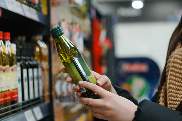 Mano femenina eligiendo aceite de oliva natural en una tienda. Concepto de comida sana, bio, vegetariana, dieta.